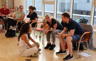 Teilnehmende sitzen im Seminarraum der il Akademie im Kreis und sprechen lachend miteinander.